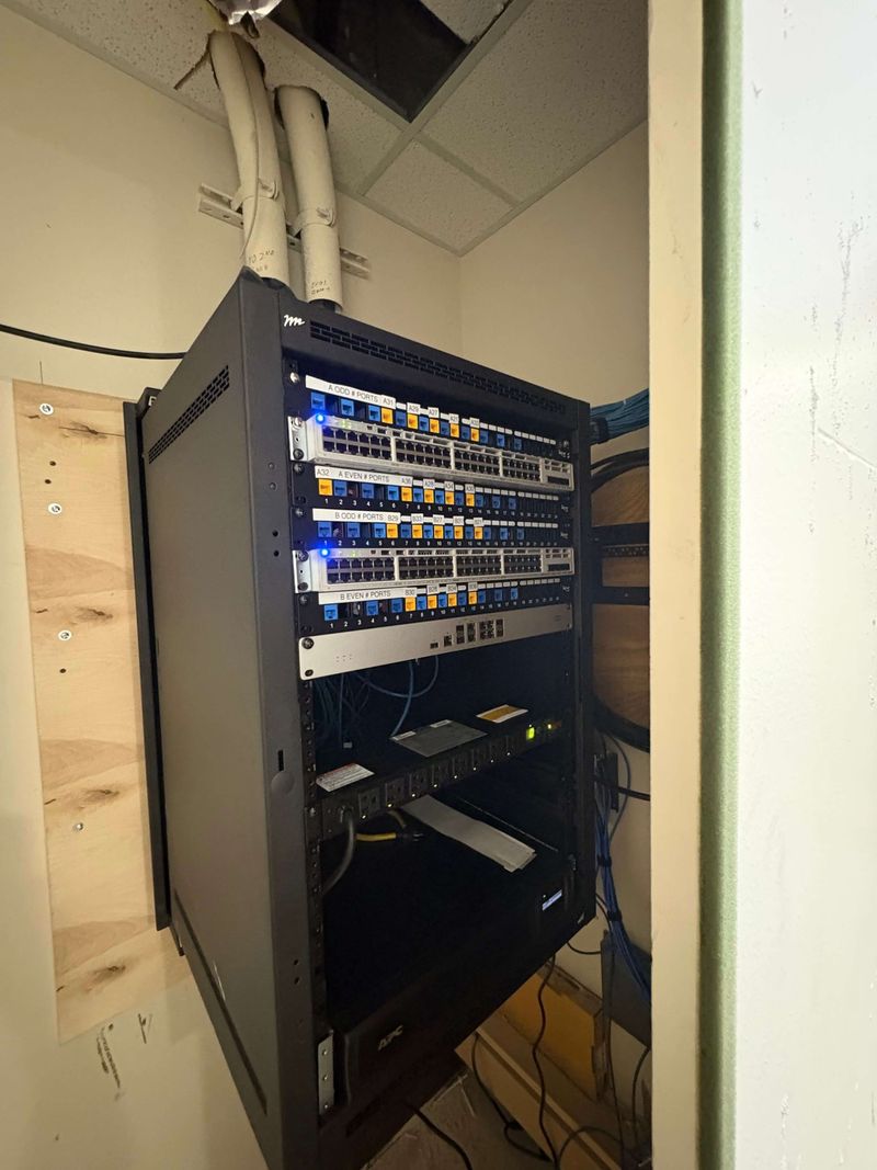 Finished network closet with a hinged wall-mounted network rack installed on a plywood backboard