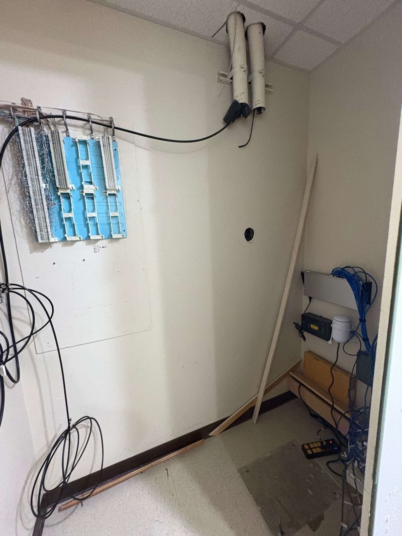 Network room wall before rack installation with loose equipment and old telephone blocks