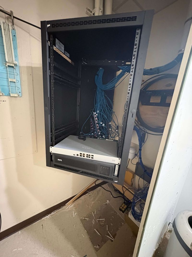 Firewall and UPS battery backup mounted in a hinged wall rack during network installation