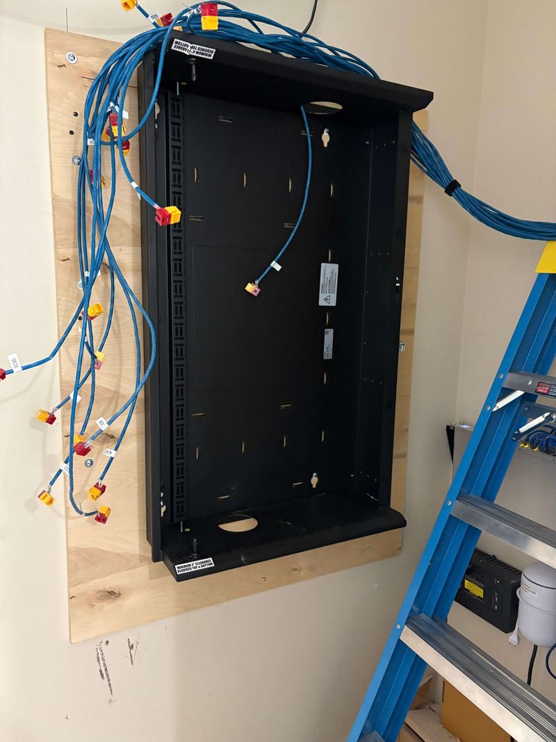 Wall-mount network rack on a plywood backboard with labeled Cat6 cable runs ready for termination