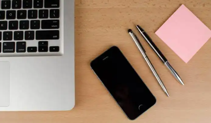 Tidy desk with a laptop, phone, pens, and a sticky note